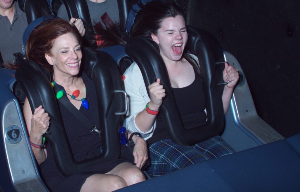 Kathryn and Ruby (white women) riding roller coaster. Kathryn is smiling while Ruby is screaming.