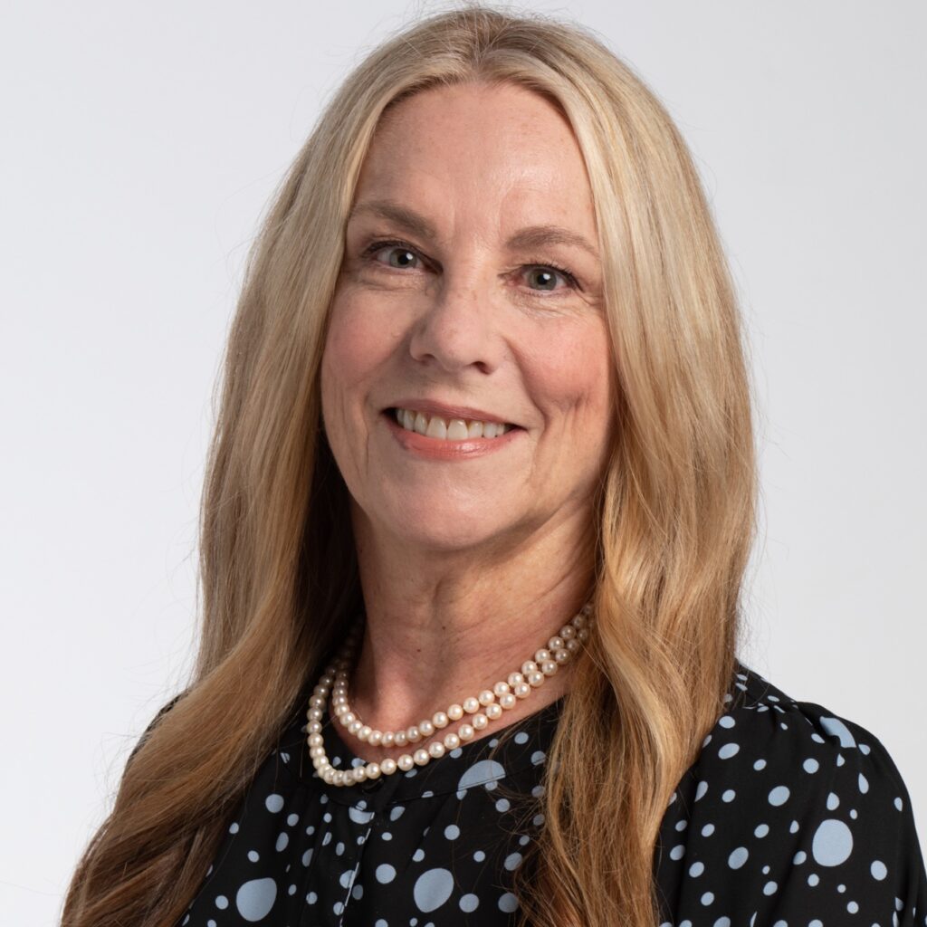 head shot of Kathryn Woodcock, with long blonde hair, black blouse with pale blue dots, pearl necklace