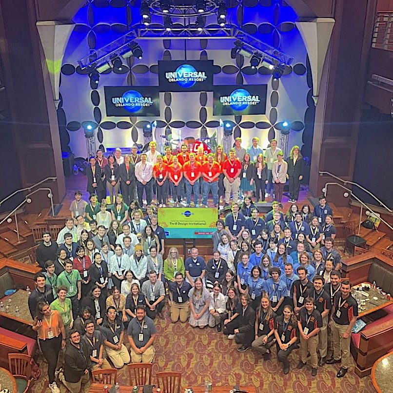 Group photo from 2022 Toronto Met U Thrill Design Invitational - 100+ people on stage and floor in front of stage pose in front of backdrops for Universal Orlando Resort / Thrill Design Invitational (photo taken from balcony)