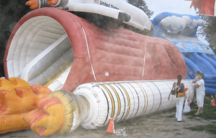 large inflatable device resembling a space shuttle is installed outdoors with two anchor points each with two tethers loosely attached
