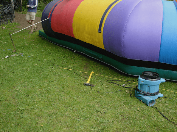 inflatable with one tether anchored in a hazardous way, another tether not anchored, and a bonus axe lying on top of extension cord during full public operation in an accessible area of the event